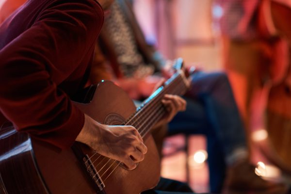 Close-up of man sitting on chair and learning to play guitar during lesson